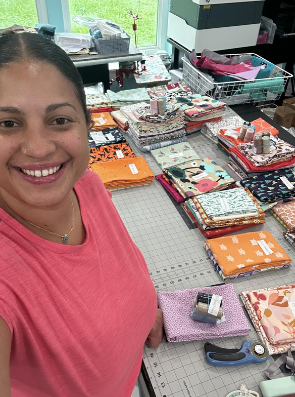 Vanessa smiling with piles of fabric bundles on table 